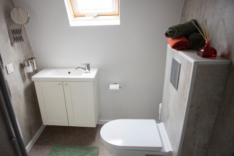 Moderne badeværelse med hvid vask, toilet, grøn måtte og sammenrullede håndklæder i De Ree en de Specht.