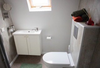 Moderne badeværelse med hvid vask, toilet, grøn måtte og sammenrullede håndklæder i De Ree en de Specht.