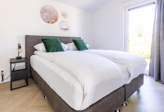 Camera moderna nello chalet Holiday Park Molenvelden 8 nei Paesi Bassi, con letto matrimoniale e cuscini verdi.