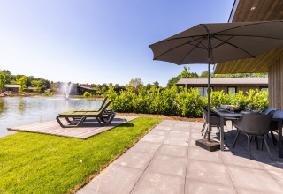 Terrasse au Holiday Park Molenvelden 8 aux Pays-Bas avec chaises longues, parasol, lac et vue sur la fontaine.