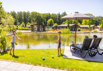 Famiglia rilassata accanto a uno stagno con chalet all’Holiday Park Molenvelden 8 in Olanda, giornata estiva.