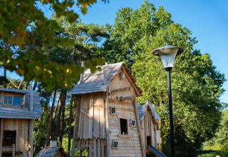 Ein rustikales Holzhaus im Wald, umgeben von hohen grünen Bäumen und einer Laterne im Vordergrund.