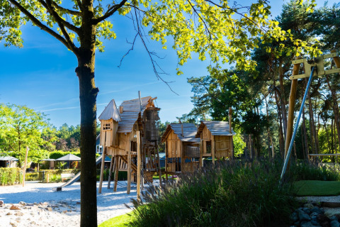 Kinderspielplatz mit rustikalen Holzhütten und Schaukeln inmitten von Bäumen an einem Chalet.