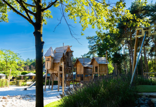 Kinderspielplatz mit rustikalen Holzhütten und Schaukeln inmitten von Bäumen an einem Chalet.