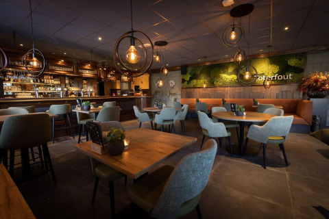 Ristorante chalet moderno con illuminazione calda, tavoli in legno, bar fornito e parete verde.