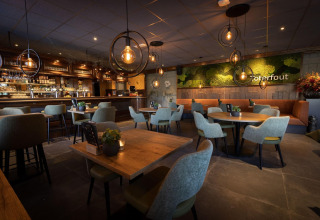 Restaurant de chalet moderne avec éclairage chaleureux, tables en bois, bar et mur végétal décoratif.