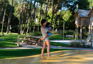 Woman holding a child at a playground in Holiday Park Molenvelden 8 in the Netherlands, trees around.