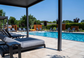 Scena presso la piscina di uno chalet moderno con lettini, patio coperto e verde circostante.