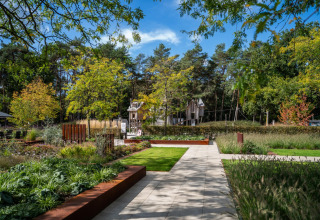 Giardino di chalet ben curato con vialetti, piante verdi e case in legno tra alberi e natura.