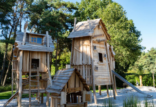 Spielplatz mit rustikalen Holzhütten und Rutsche im Grünen, gelegen bei einem Chalet im Sommer.