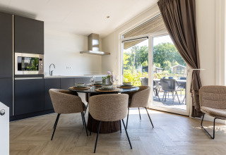 Cucina e zona pranzo moderne in chalet con ampie finestre e terrazza al Holiday Park Molenvelden 7, Paesi Bassi.