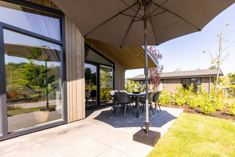 Hyggelig terrasse ved Holiday Park Molenvelden 7 med stor parasol, havebord og moderne træchalet.