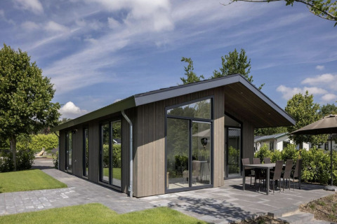 Moderne chalet med store vinduer ved Holiday Park Molenvelden 7, omkranset af grønne haver og terrasse.