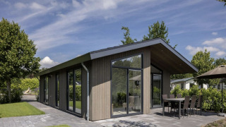 Moderne chalet med store vinduer ved Holiday Park Molenvelden 7, omkranset af grønne haver og terrasse.