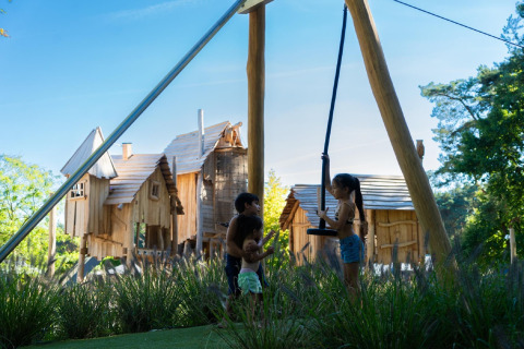 Kinder spielen an einer Schaukel vor rustikalen Holzhütten im Holiday Park «Molenvelden 7» in den Niederlanden.