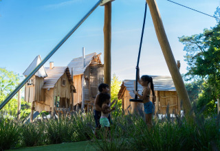 Niños juegan cerca de un columpio con cabañas de madera al fondo en Holiday Park «Molenvelden 7», Países Bajos.
