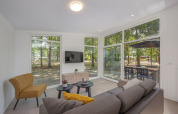 Sala de estar luminosa en una cabaña, con muebles modernos, grandes ventanales y vista al bosque y terraza.