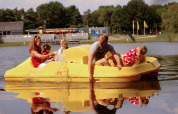 Una familia disfruta en un bote a pedales amarillo durante su estancia en un alojamiento glamping junto al lago.