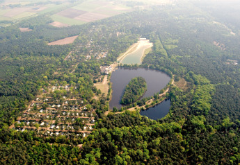 Luchtfoto van een lodge aan een meer, omringd door bos, huisjes en uitgestrekte groene velden.