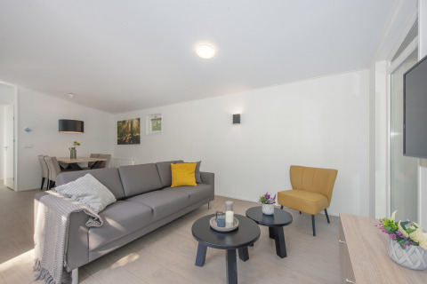 Modern lodge living area with a gray sofa, yellow chair, nesting tables, and a dining area in the back.