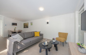 Modern lodge living area with a gray sofa, yellow chair, nesting tables, and a dining area in the back.
