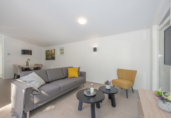 Acogedora sala en una lodge con sofá gris, sillón amarillo, mesas redondas y comedor al fondo.