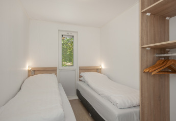 A small lodge bedroom with two single beds, a wardrobe with hangers, and a narrow window at the end.