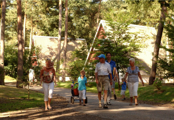 Una familia pasea por un sendero frente a cabañas entre árboles, disfrutando de un día al aire libre.