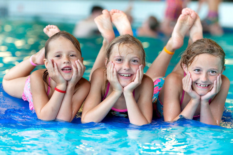 Tre glade børn leger sammen i en swimmingpool på et glampingophold, smilende og afslappede.