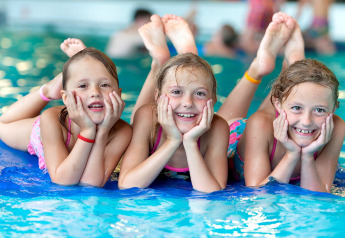 Tres niños sonrientes se divierten juntos en la piscina durante una estancia en un alojamiento glamping.