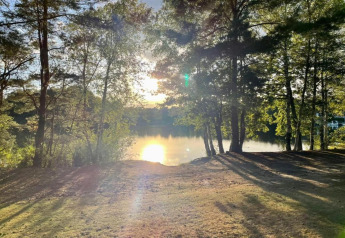 Vista del atardecer desde un alojamiento glamping junto a un lago, con árboles y césped cerca del agua.