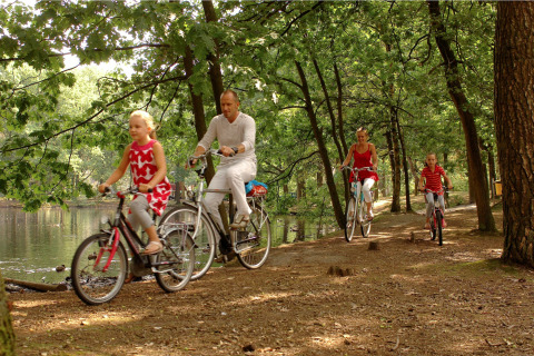 Familia pasea en bicicleta junto a un lago entre árboles durante una estancia en glamping.