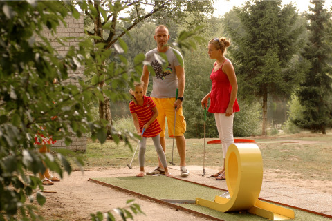 Familie spiller minigolf i grønne omgivelser på et glamping-sted, eventyr og afslapning udendørs.