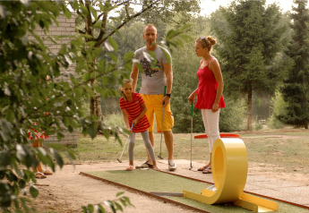 Famille jouant au mini-golf ensemble lors d’un séjour glamping, entourée de nature et d’arbres verts.