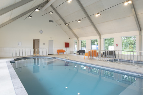 Indendørs swimmingpool i et lyst glampingområde med moderne møbler og store vinduer med udsigt.