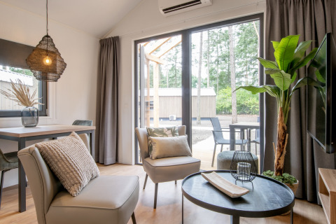 Modernes Wohnzimmer in einem Tiny House mit großen Fenstern und Blick auf einen Wald in den Niederlanden.