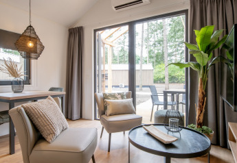 Salon moderne d’une tiny house avec grandes baies vitrées et vue sur la forêt aux Pays-Bas.