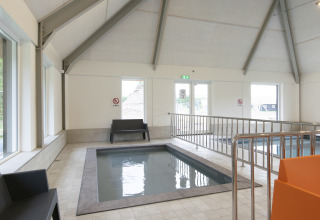 Area piscina interna con sedute moderne e grandi finestre in una struttura glamping accogliente.