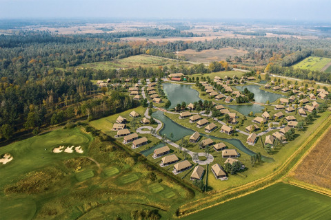 Vista aerea di un resort glamping con cottage moderni, laghetti e campo da golf immersi nel verde.
