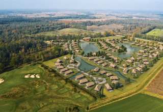 Vista aérea de alojamientos glamping con cabañas modernas, lagos, vegetación y campo de golf cercano.