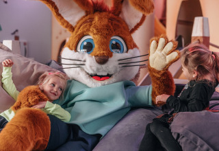 Deux enfants partagent un moment joyeux avec une mascotte lapin géante dans un hébergement glamping.
