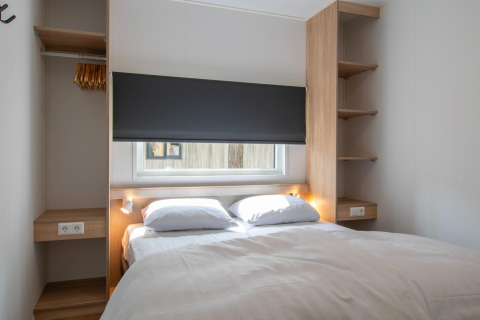 Modernes Schlafzimmer in einer Lodge mit Doppelbett, Fenster, offenem Schrank und Holzregalen.