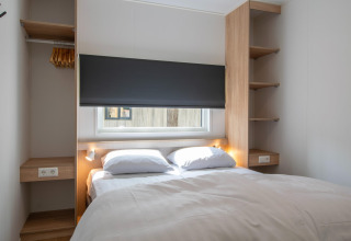 Chambre moderne dans un lodge avec lit double, fenêtre, penderie ouverte et étagères en bois éclairées.