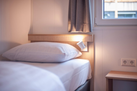 Modernes Bett mit weißer Bettwäsche im Forest Park 't Wolfsven 19, Niederlande, mit Fenster und Leselampe.
