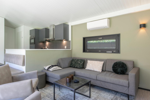 Salón moderno con sofá gris, cocina abierta y aire acondicionado en una cabaña en los Países Bajos.