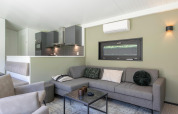 Moderne opholdsstue med grå sofa, åbent køkken og vægmonteret aircondition i en lodge i Holland.