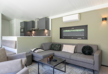 Modernes Wohnzimmer mit grauem Sofa, offenem Küchenbereich und Klimaanlage in einer niederländischen Lodge.