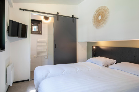Modern bedroom with double bed, TV, and sliding door to bathroom at Forest Park 't Wolfsven 16, Netherlands.