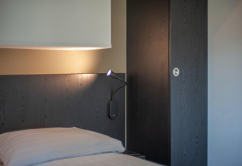 Modernes Schlafzimmer im Forest Park 't Wolfsven 16 mit Bett, Leselampe und dunkler Wandverkleidung.