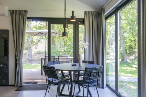 Salle à manger moderne avec grandes fenêtres et vue sur la forêt à Forest Park 't Wolfsven 15, Pays-Bas.